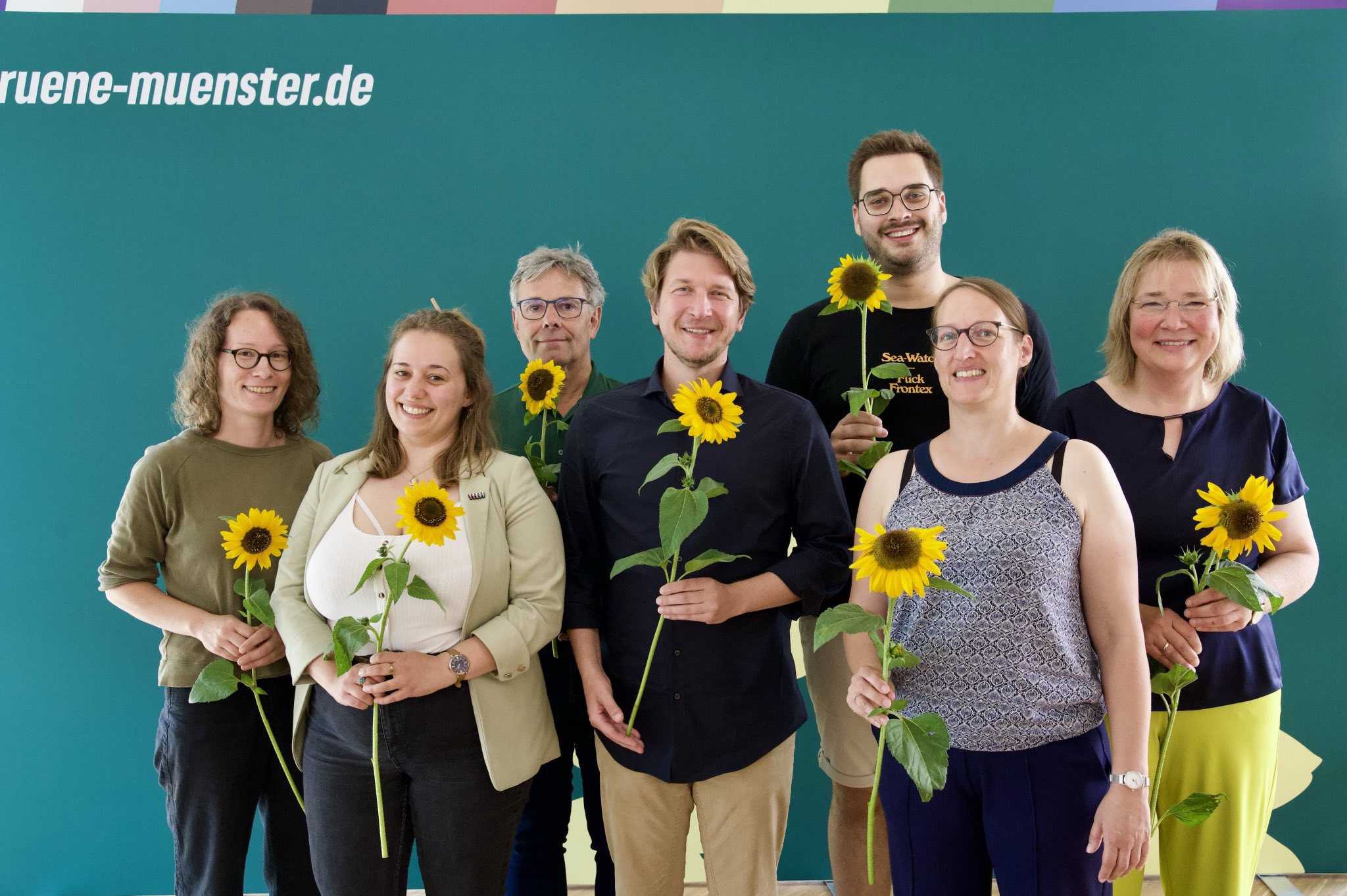 Auf dem Bild stehen Sonja Völker, Katie Foreman, Fritz Bachmair, Jörg Rostek, Lukas Färber, Birgit Wolters und Almut Wiemers vor einem Grünen Hintergrund