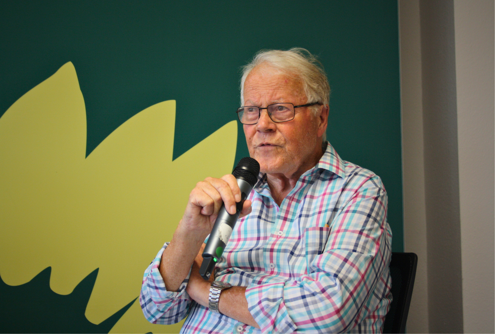 Winfried Nachtwei mit einem Mikrofon in der Hand von Grünem Hintergrund
