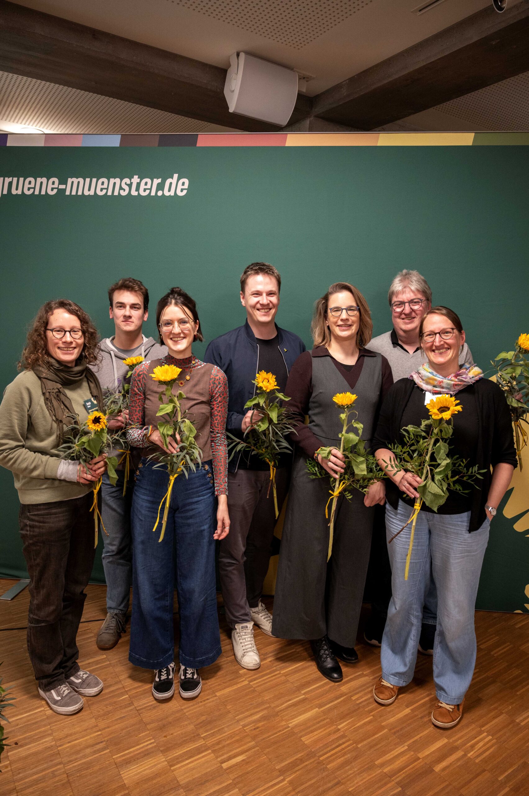 Der neue Vorstand steht vor einem Grünen Hintergrund und hält Sonnenblumen in der Hand
